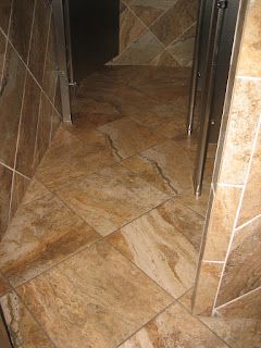 Tiled bathroom floor and walls in shades of brown, leading to open doorway.