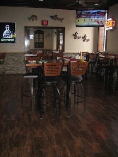 Interior restaurant shot: tables, chairs, TV, neon sign, wood flooring.