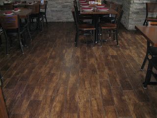 Restaurant interior with brown wood-look tiled floor. Tables and chairs are set for dining.