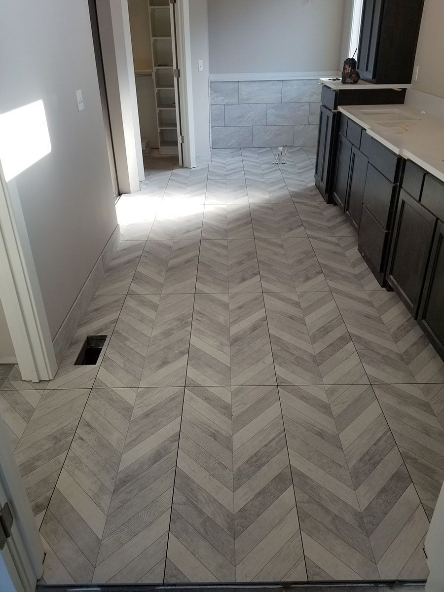 Herringbone tile floor in a room, leading to a doorway, with dark cabinets and a closet visible