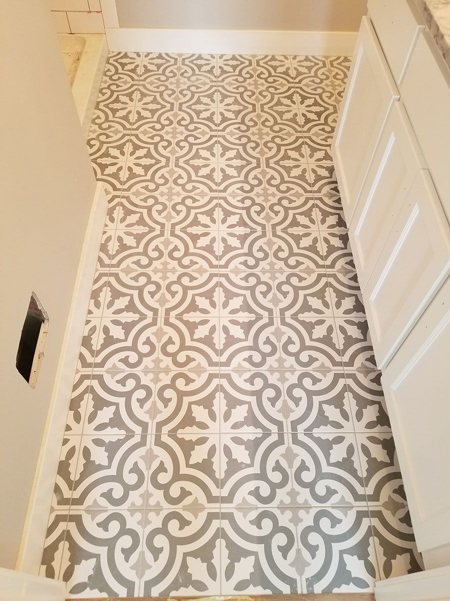 Gray and white patterned tile flooring in a bathroom, next to a white cabinet and wall