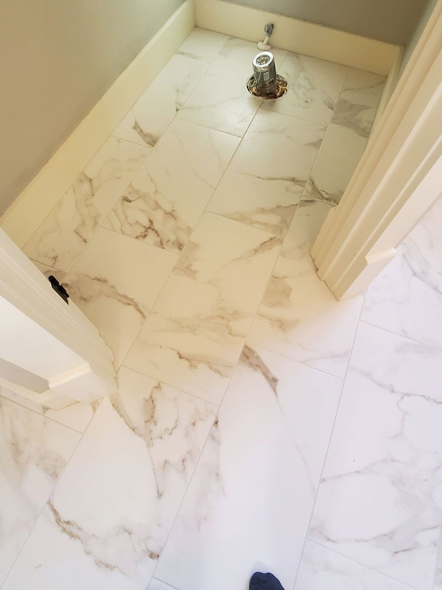 White and beige marble tiled floor in a bathroom, with a toilet flange visible and trim around the edges