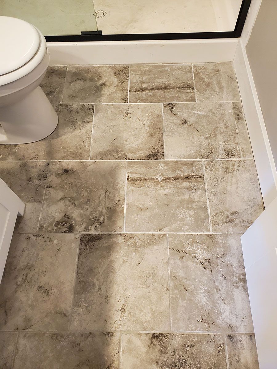 Bathroom floor with neutral-colored rectangular tiles, near a toilet and shower
