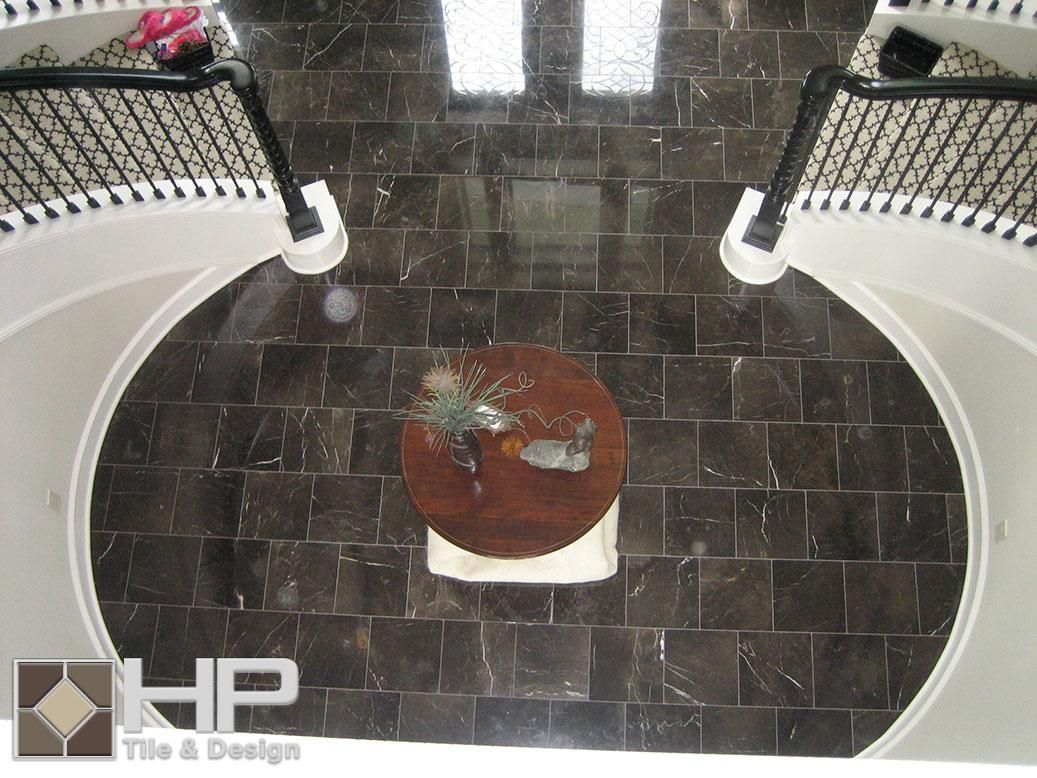 Overhead view of a grand foyer with dark tiled floor, curved white staircases, and a round table centerpiece