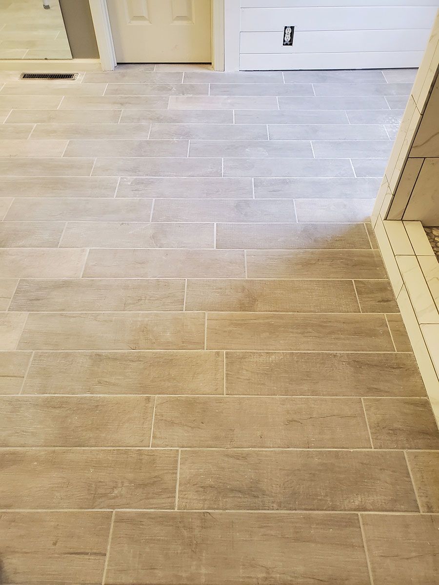 Tan rectangular tile floor in a room, partially lit, next to a doorway and a white wall