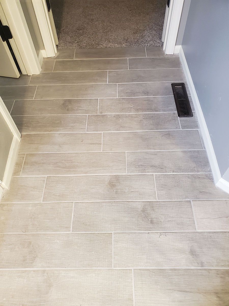Gray tiled floor transitioning to a gray carpeted hallway. Air vent on right. White trim and door frames