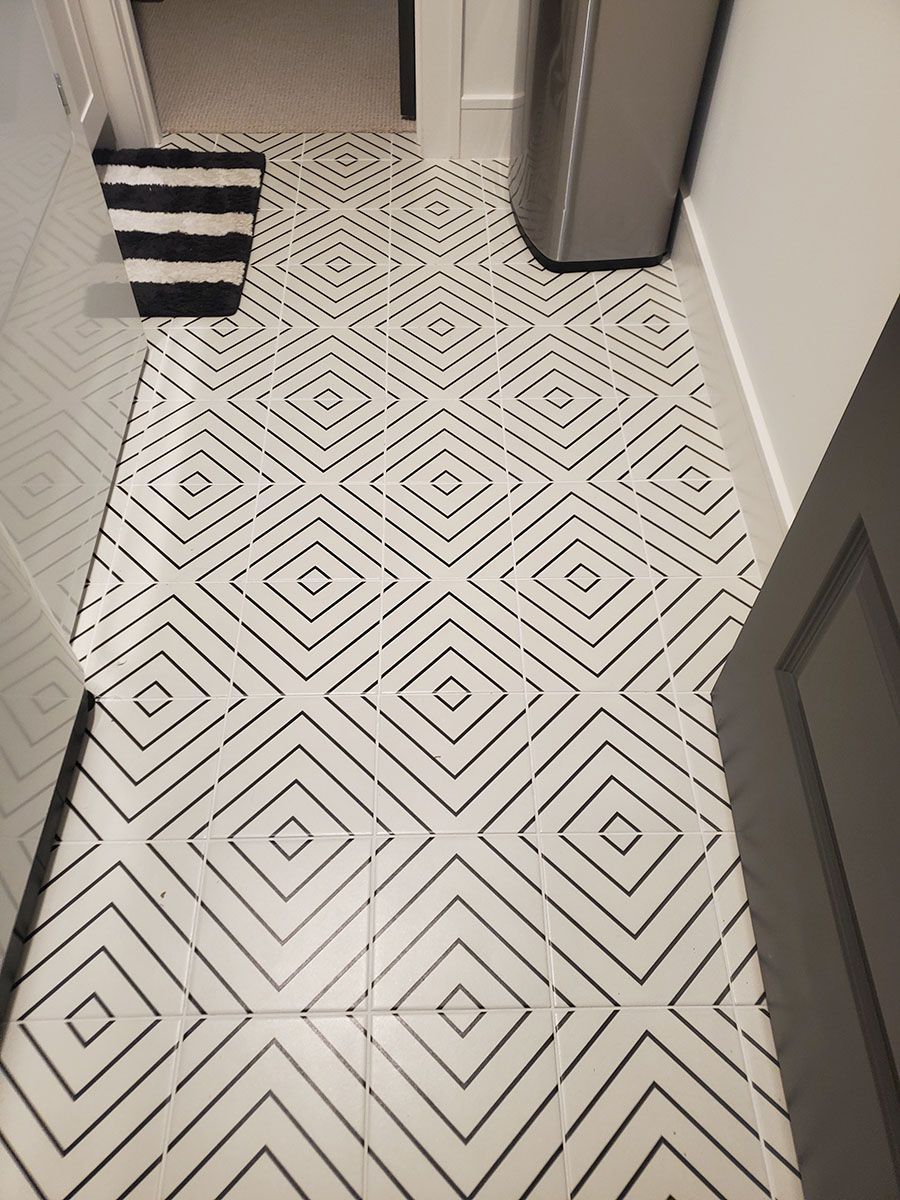 White floor tiles with black diamond patterns in a hallway, laundry machine on the right, black and white rug on the left