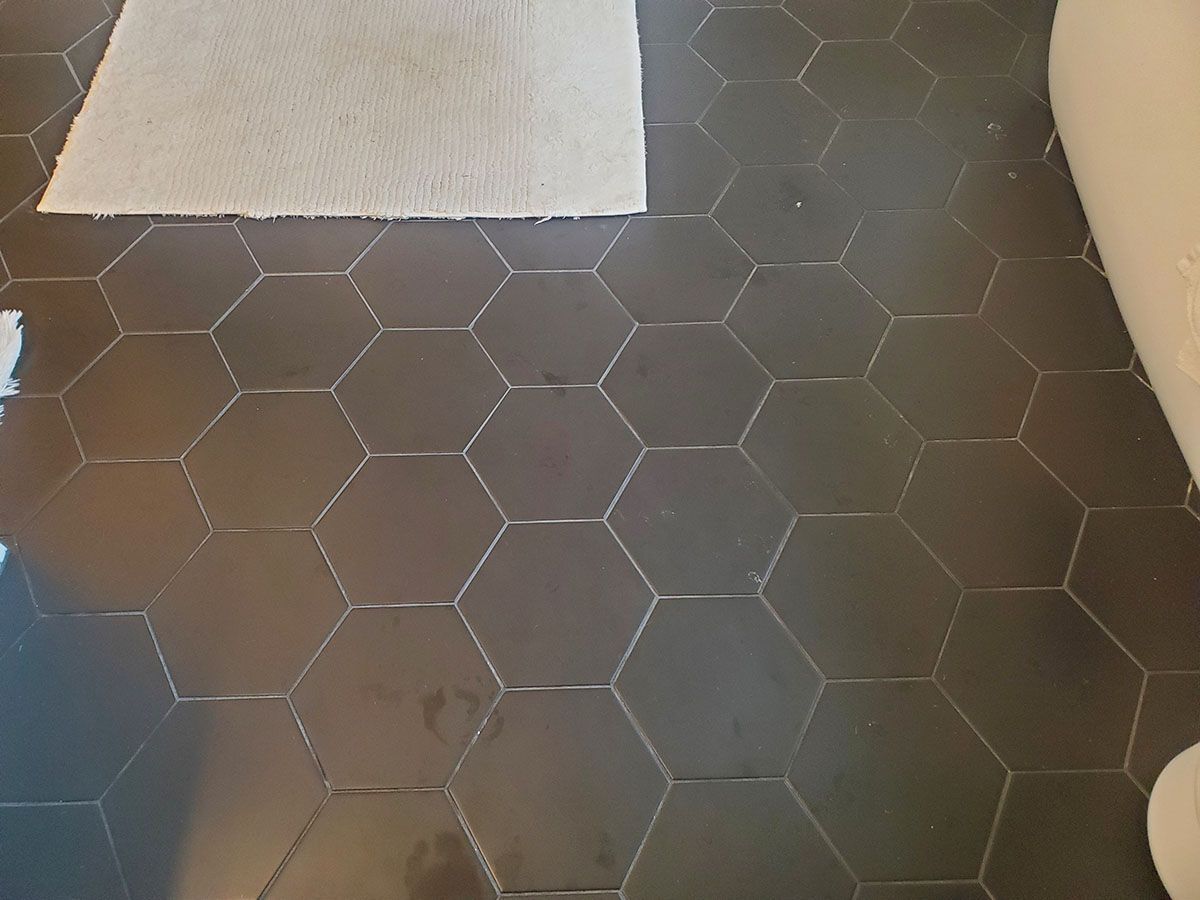 Dark hexagonal tile floor with a light-colored bath mat and a roll of white fabric