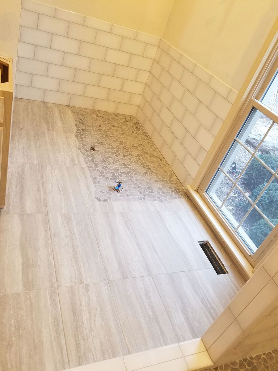 Bathroom with light-colored tile flooring, shower walls, and a mosaic shower floor