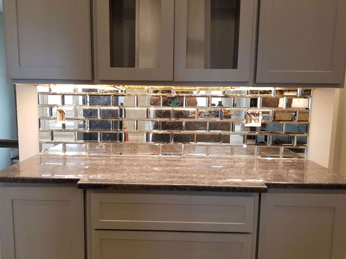Gray kitchen cabinets with a mirrored tile backsplash and granite countertop