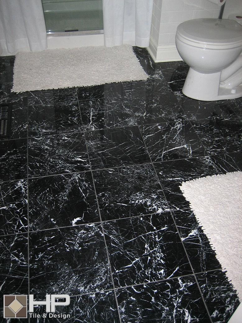 Black and white marble tile bathroom floor with white bath rugs and toilet