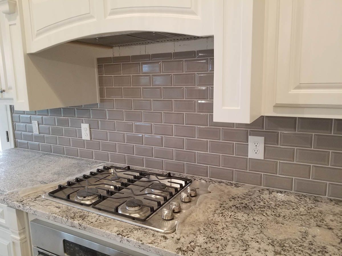 Kitchen with granite countertops, grey subway tile backsplash, and white cabinets