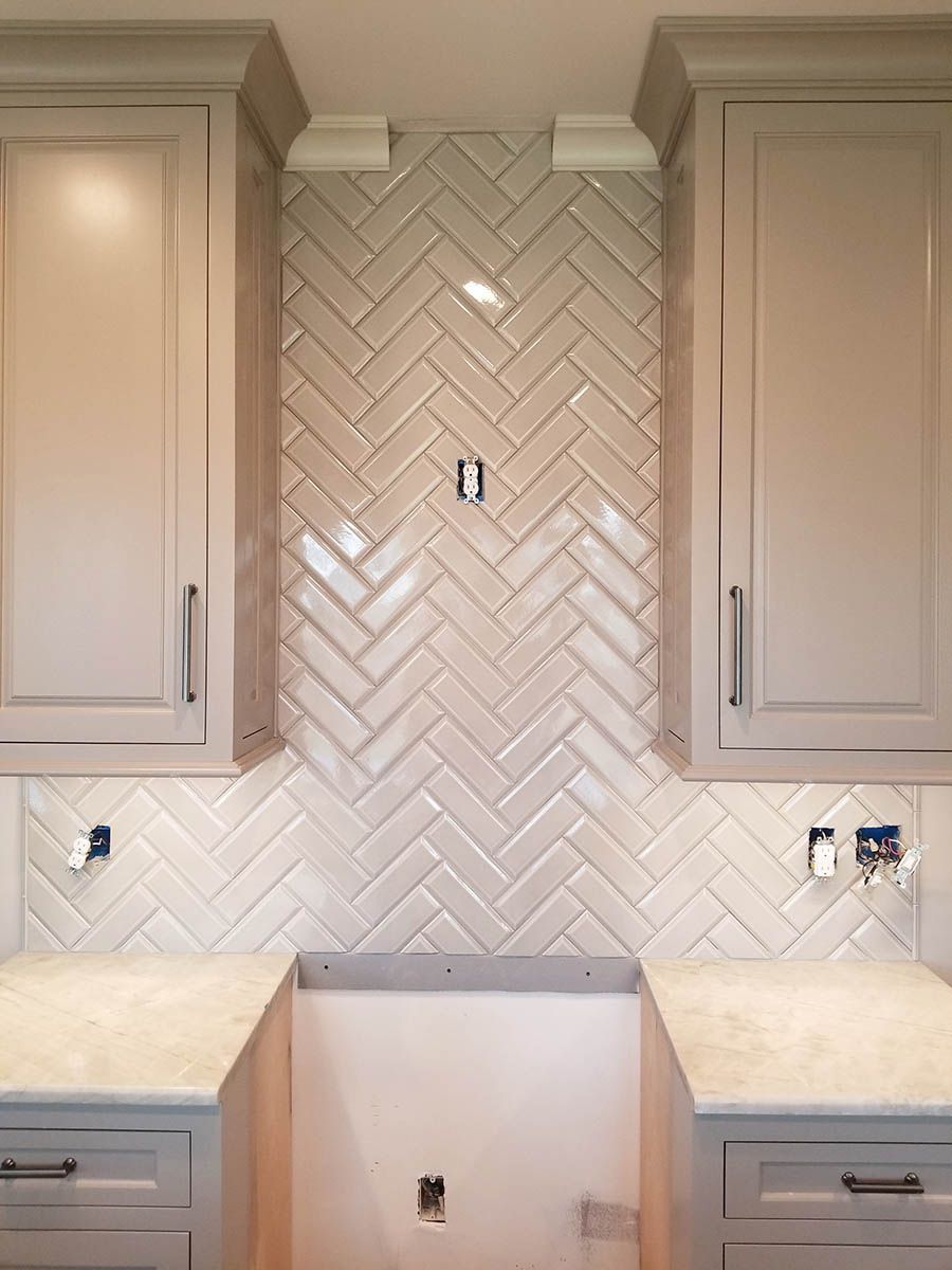 Herringbone tile backsplash in a kitchen, between two cabinets, with light countertops