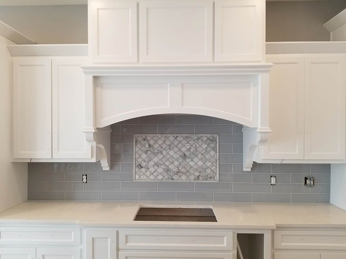 White kitchen cabinets with gray backsplash and range hood over stovetop
