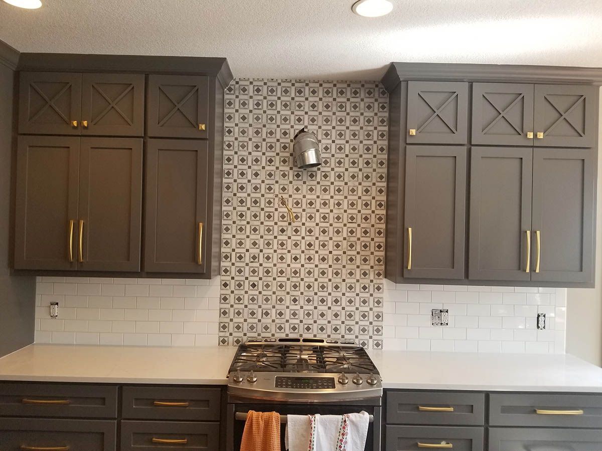 Gray kitchen cabinets with gold hardware, white countertops, and patterned backsplash above a stove