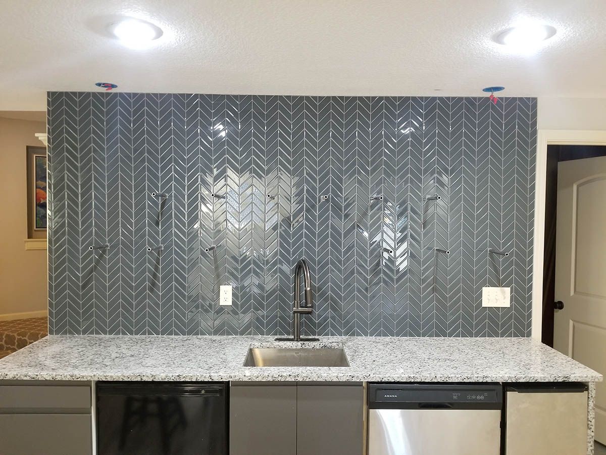 Kitchen with gray tile backsplash, granite countertop, stainless steel sink, and appliances