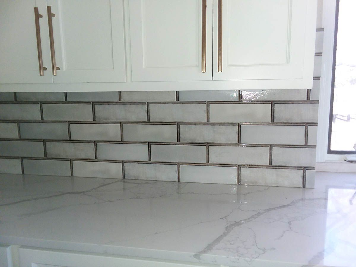 White kitchen cabinets above a light gray brick-patterned backsplash and marble countertop