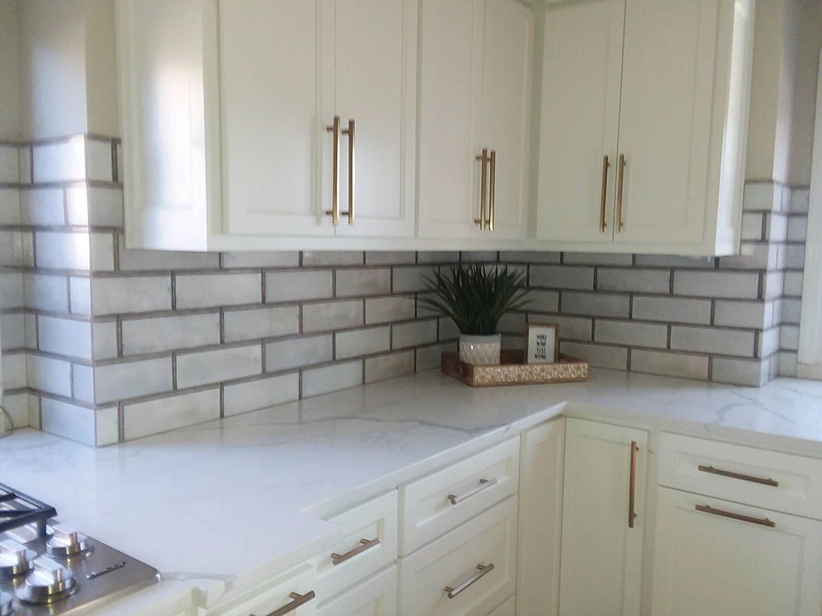 White kitchen corner with marble countertops, white cabinets, and subway tile backsplash