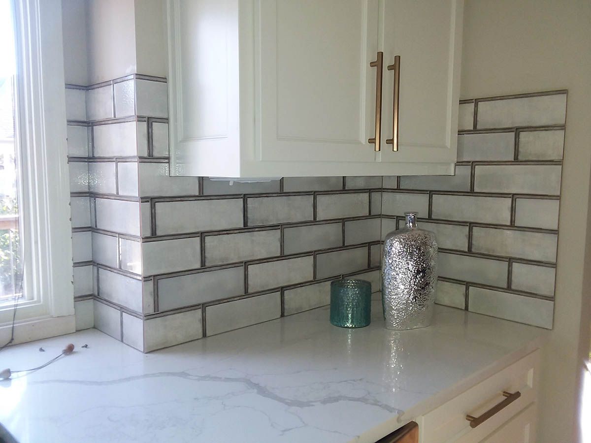 Kitchen with white cabinets, marble-look countertop, and white subway tile backsplash with silver grout