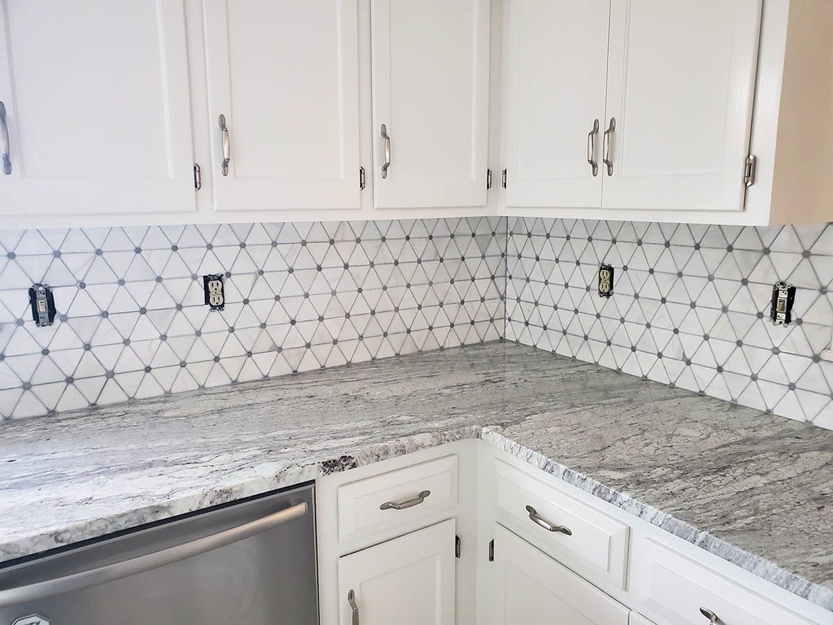 White kitchen with geometric tile backsplash, granite countertops, and white cabinets