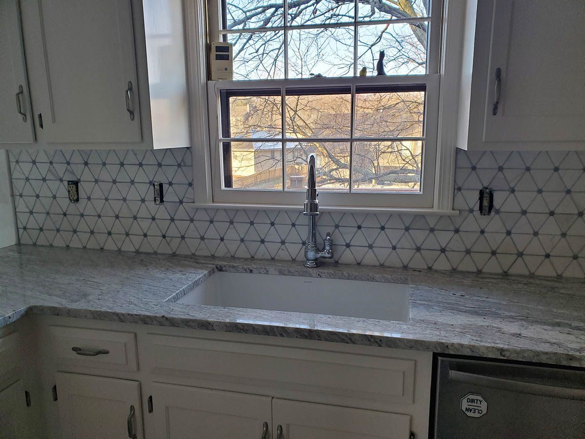 Kitchen with white cabinets, triangle tile backsplash, granite countertop, and a window