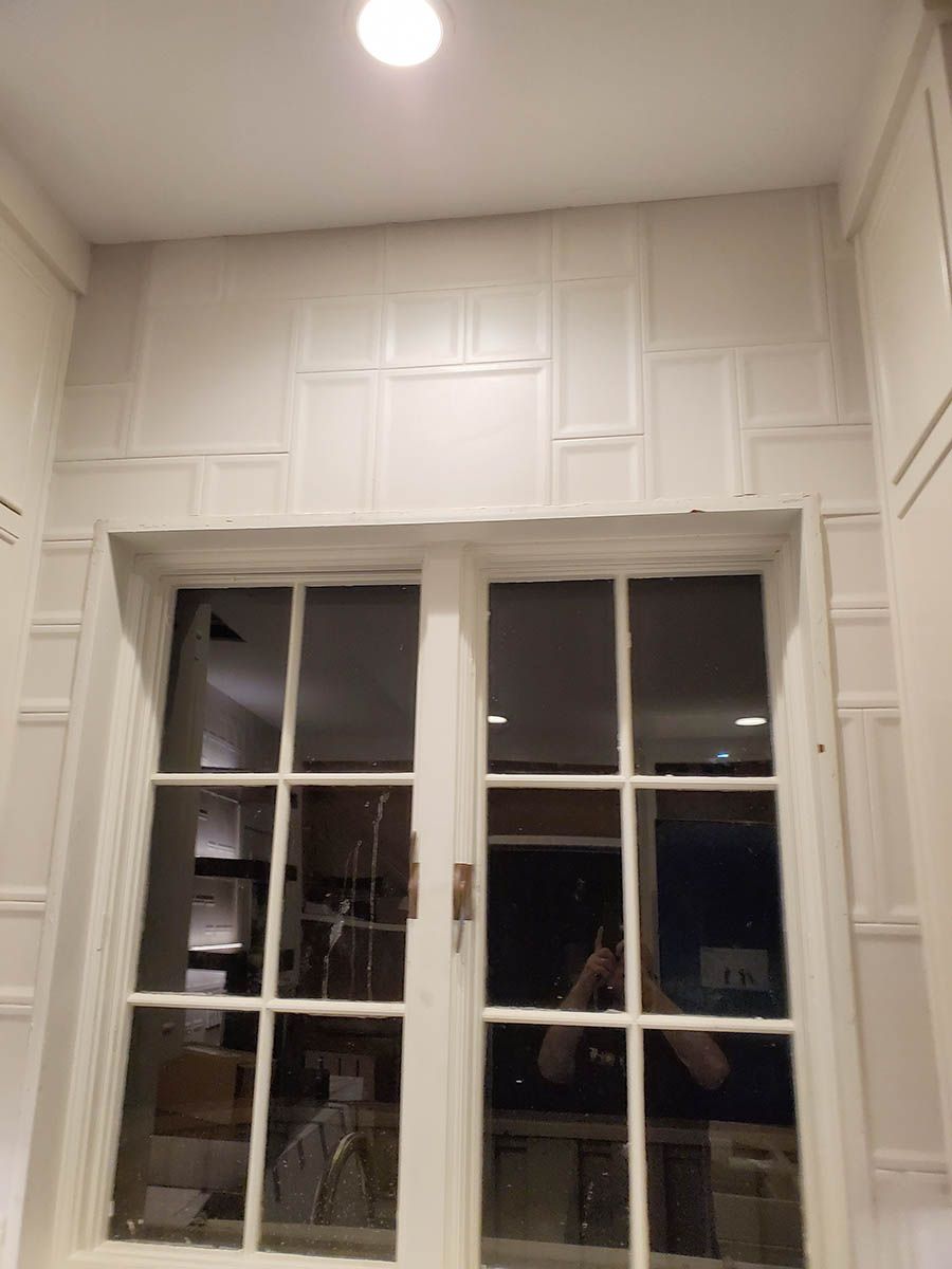 White-framed window with multiple panes, above which are white wall panels