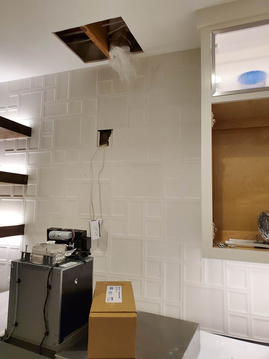 Steam billowing from a ceiling opening. White tiled wall, cabinet, box, and appliance in a room