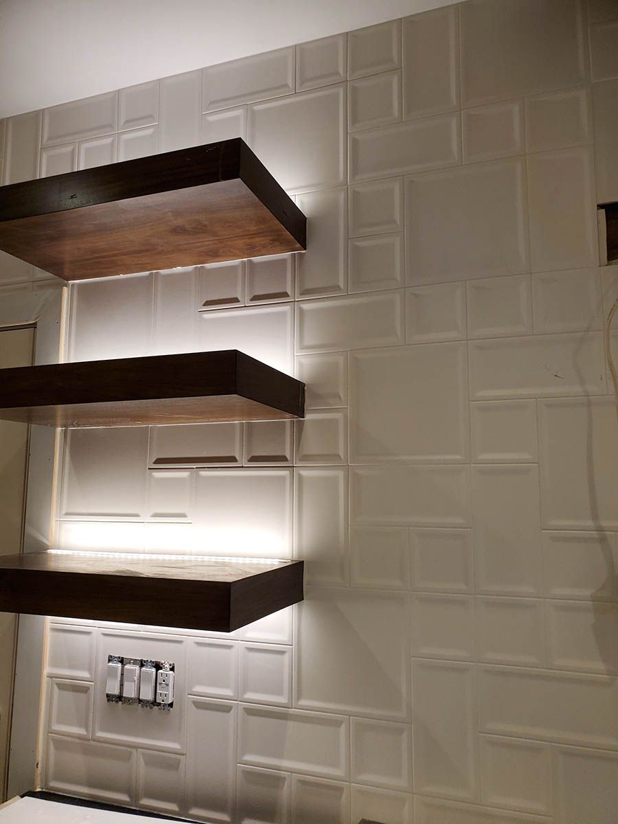Three wooden shelves with under-shelf lighting, mounted on a textured white wall