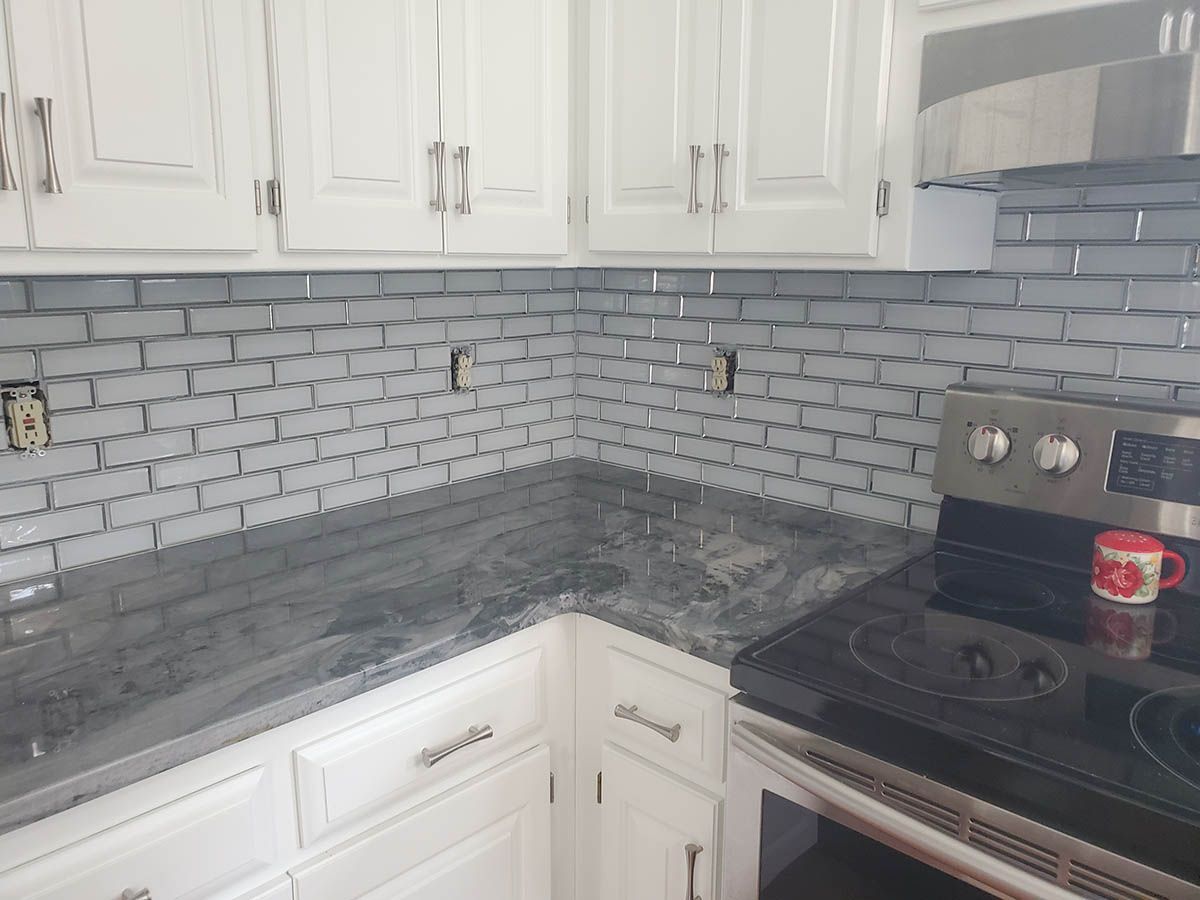 Kitchen corner with white cabinets, dark gray countertops, and gray brick-like backsplash tiles