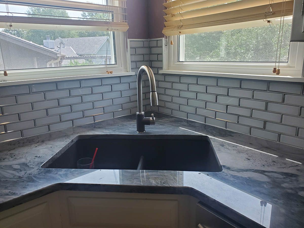 Corner kitchen sink with gray brick-patterned backsplash, granite countertop, and chrome faucet