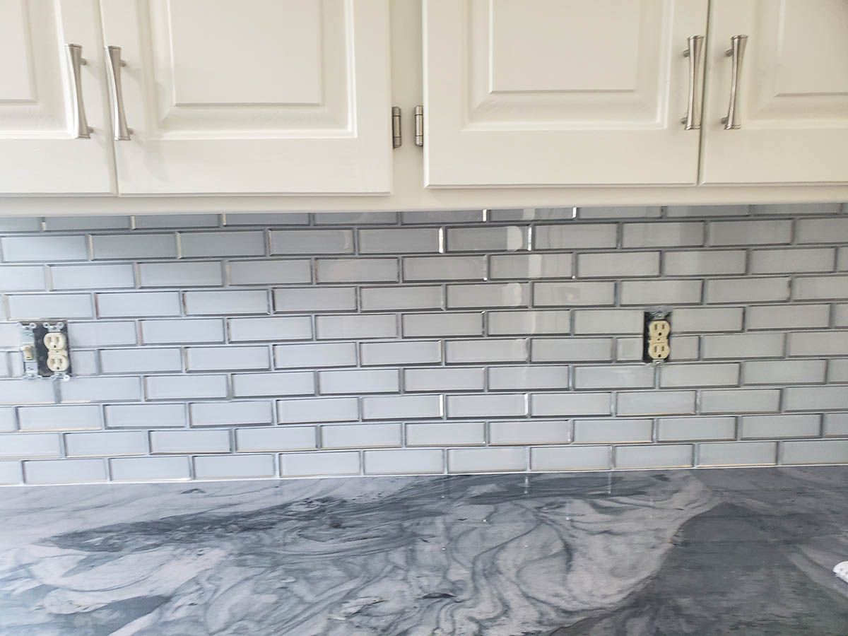 White brick-style backsplash above a dark countertop, below white cabinets