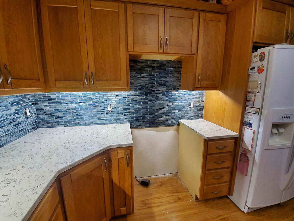 Kitchen with wooden cabinets, blue backsplash, and white countertop under construction