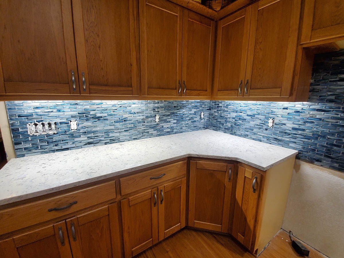 Kitchen with light wood cabinets, white countertops, and blue tiled backsplash