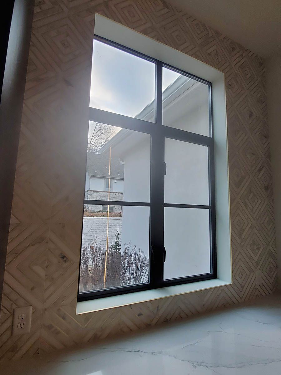 Window with black grid, surrounded by patterned tile, overlooking a cloudy sky and house