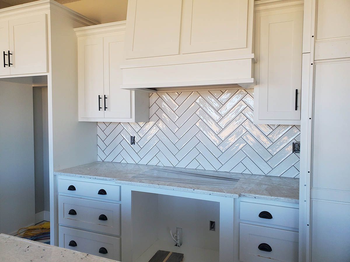 White kitchen cabinets with black hardware and herringbone backsplash