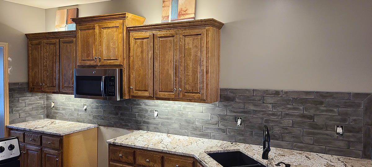 Kitchen with wood cabinets, stone backsplash, and white countertops