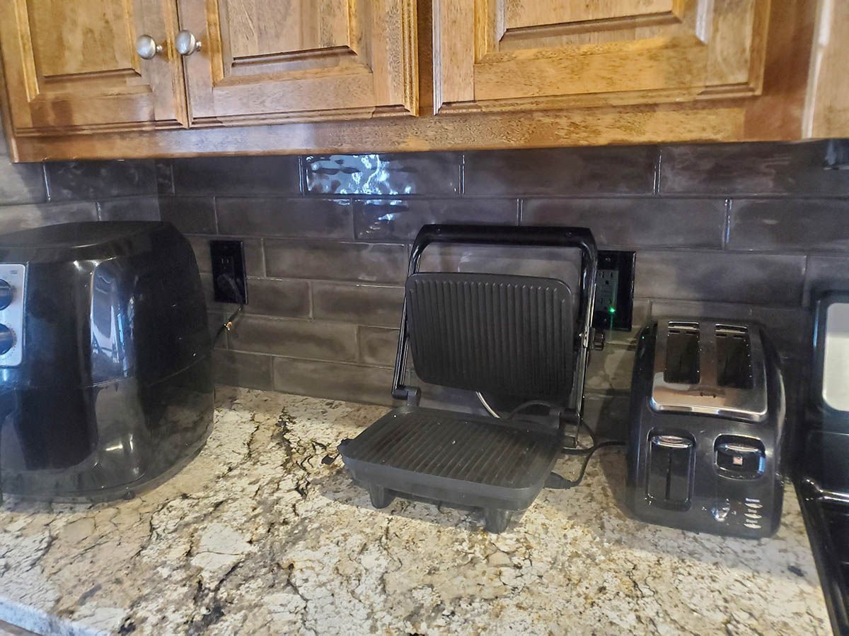 Kitchen countertop with an air fryer, grill, and toaster, with outlets on the backsplash