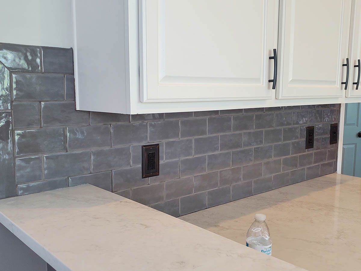Gray tiled kitchen backsplash with white cabinets and dark electrical outlets