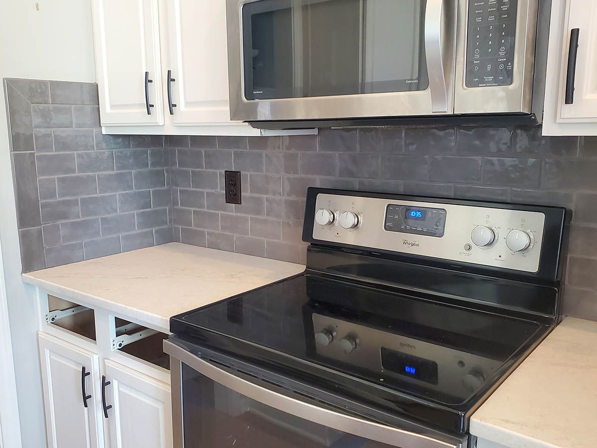 Kitchen with white cabinets, gray backsplash, stainless steel appliances, and white countertop