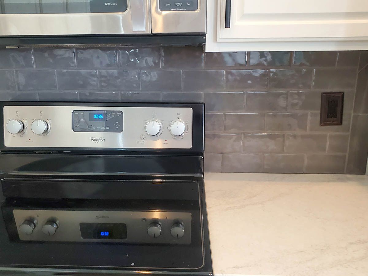 Kitchen backsplash with stove and microwave; gray subway tile, white countertop, white cabinets, stainless steel appliances
