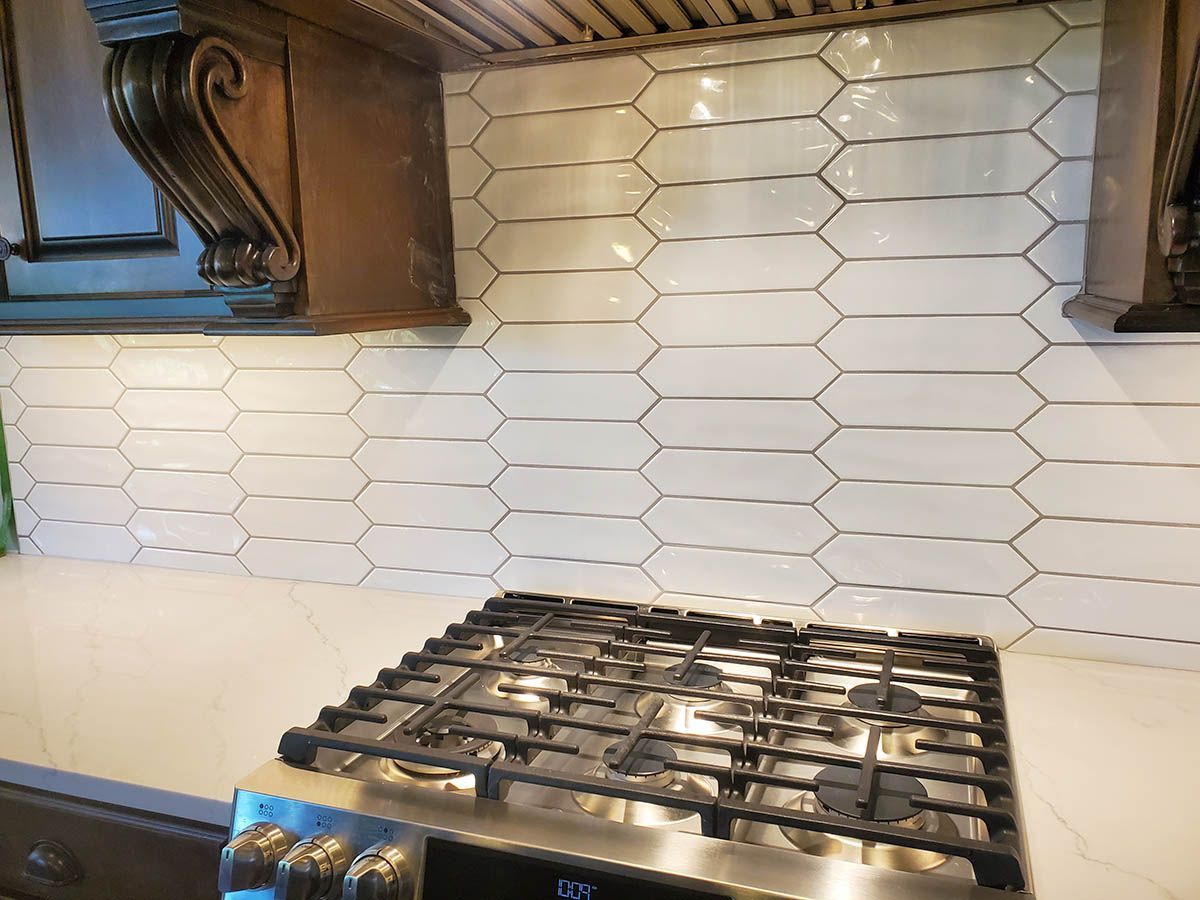 Kitchen backsplash with white geometric tiles above a gas stove and white countertop