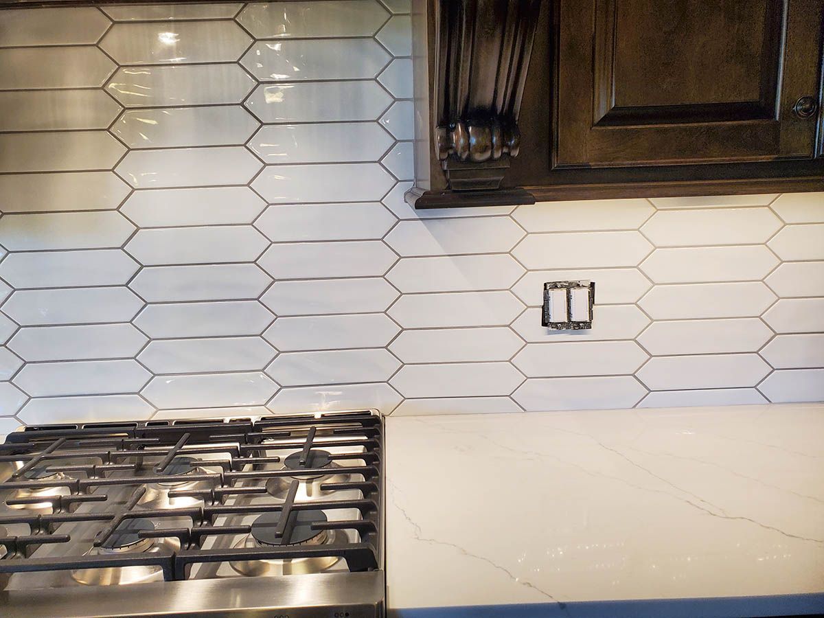 White and black elongated hexagon tile backsplash in a kitchen, above a gas stovetop and countertop