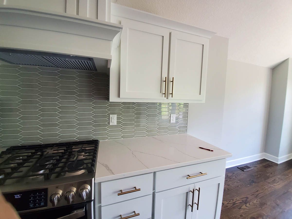 Kitchen with white cabinets, light countertops, gas stove, and patterned backsplash