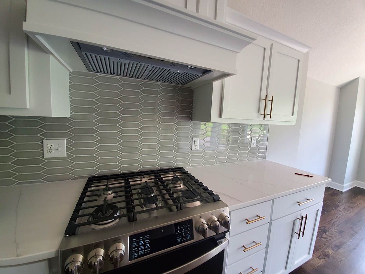 Kitchen with gray backsplash, white cabinets, stainless steel stove, and white countertops