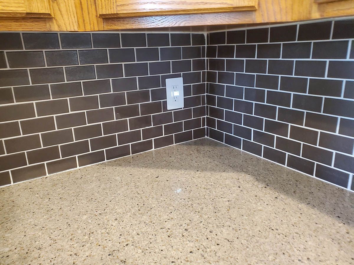 Dark brick backsplash above a speckled countertop, with a light switch in the center