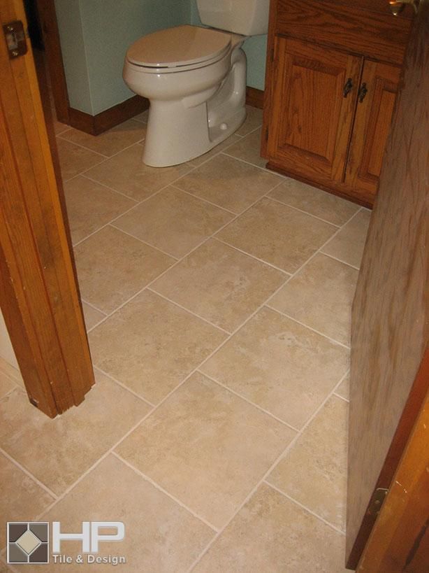 Beige tiled bathroom floor with toilet, cabinets, and doorway