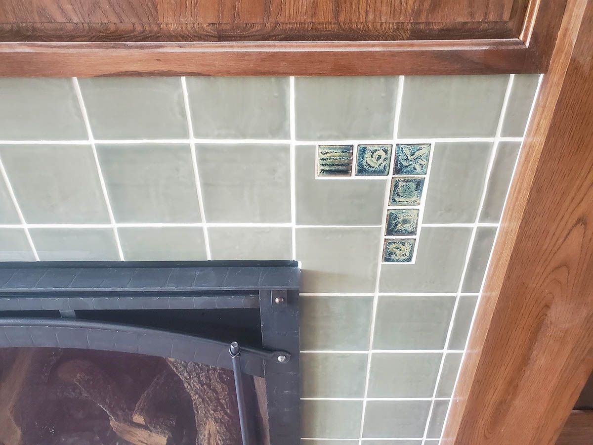 Green tiled wall with decorative tiles near a fireplace