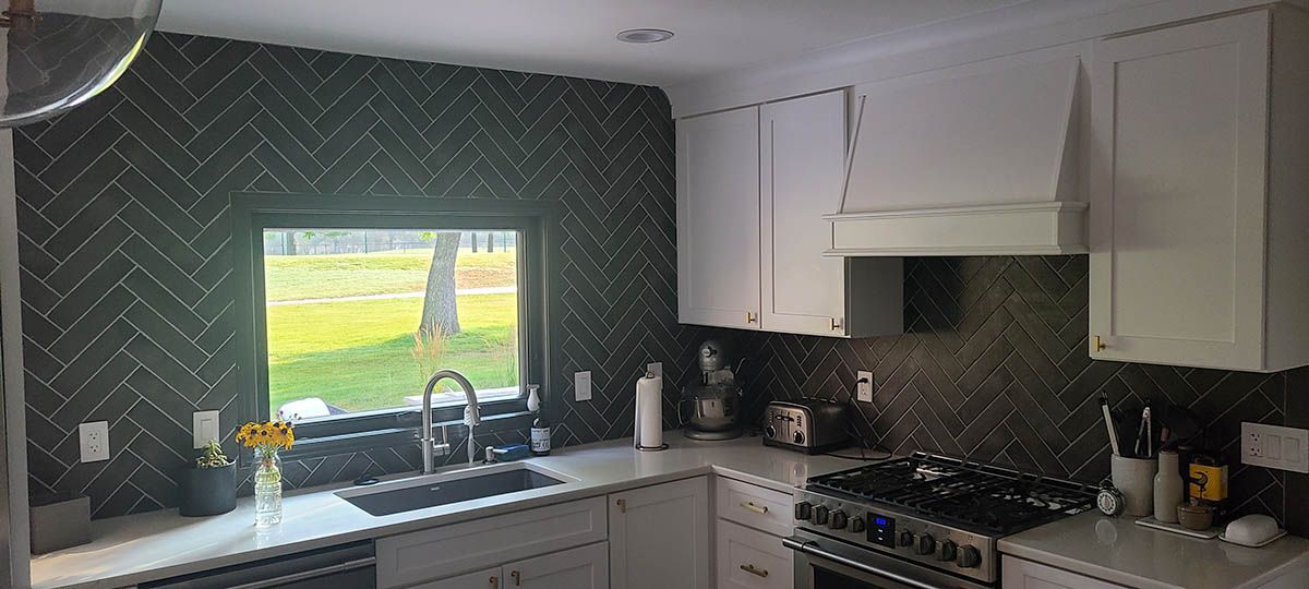 Kitchen with dark backsplash, white cabinets, and a view of a grassy area through a window