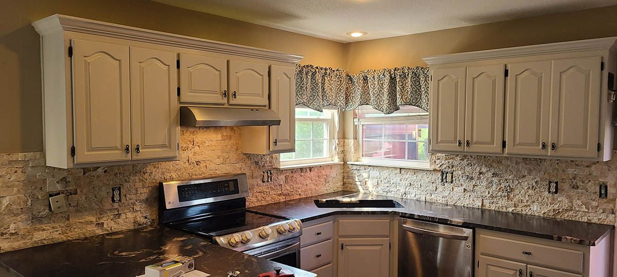 Kitchen with light cabinets, backsplash, stove, and a window with a curtain