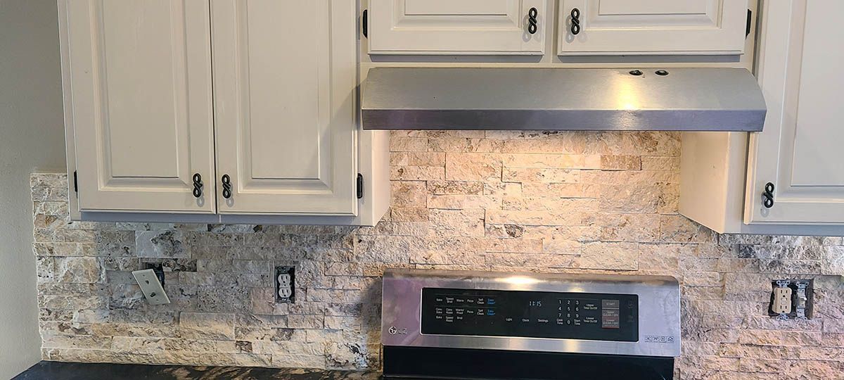 Kitchen with white cabinets, stainless steel range hood, and textured backsplash